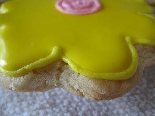 Close up of an eggless sugar cookie decorated to look like a flower with yellow Royal icing.