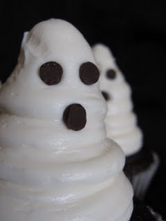 Close up of chocolate cupcakes topped with white buttercream frosting decorated to look like ghost faces.