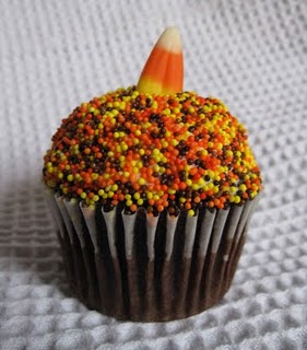 A chocolate cupcake decorated with Halloween-themed sprinkles and topped with a candy corn piece.