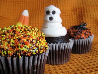 Three Halloween cupcakes with various decoration themes, including candy corn, a ghost, and spiders.