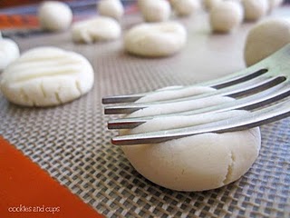 A fork is used to imprint the tops of meltaway cookie dough balls laid out on a baking sheet.