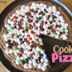 Overhead view of a cookie pizza in a pan with a slice removed