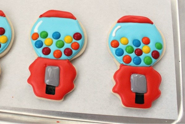 Two gumball machine decorated sugar cookies with gray dispenser