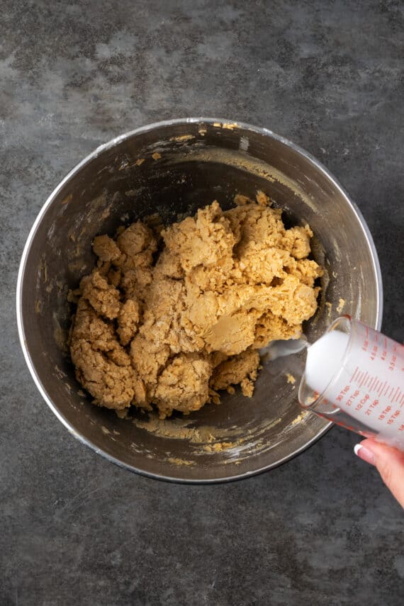 Milk being poured into peanut butter frosting in a metal mixing bowl.