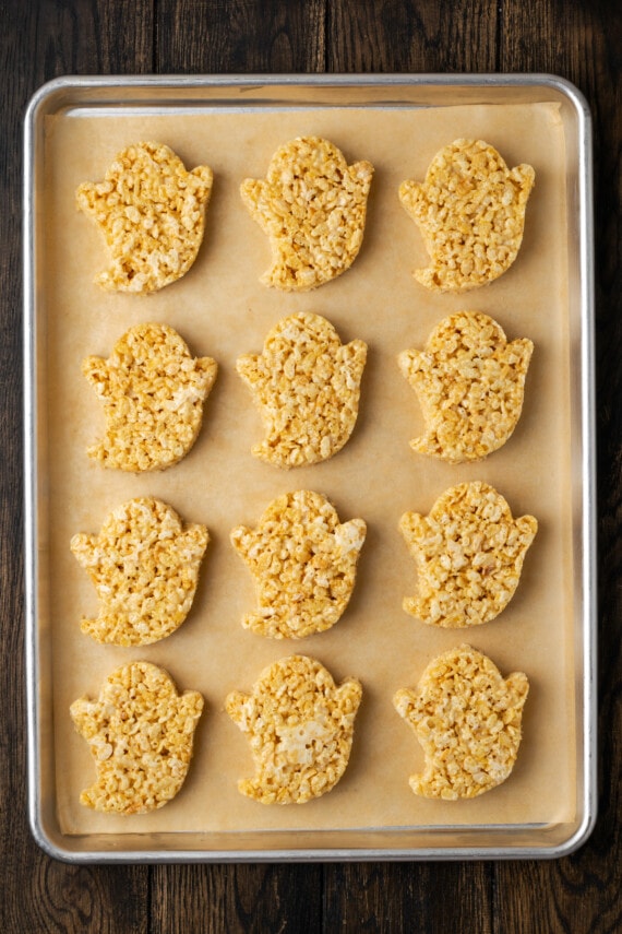Cutout rice krispie treat ghosts arranged in rows on a parchment-lined baking sheet.