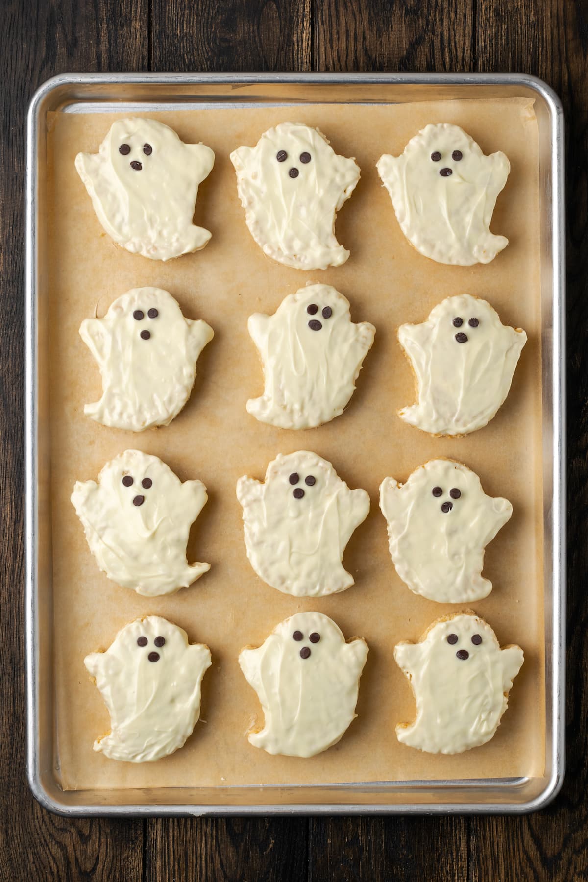 Halloween rice krispie treat ghosts dipped in white chocolate arranged in rows on a baking sheet.