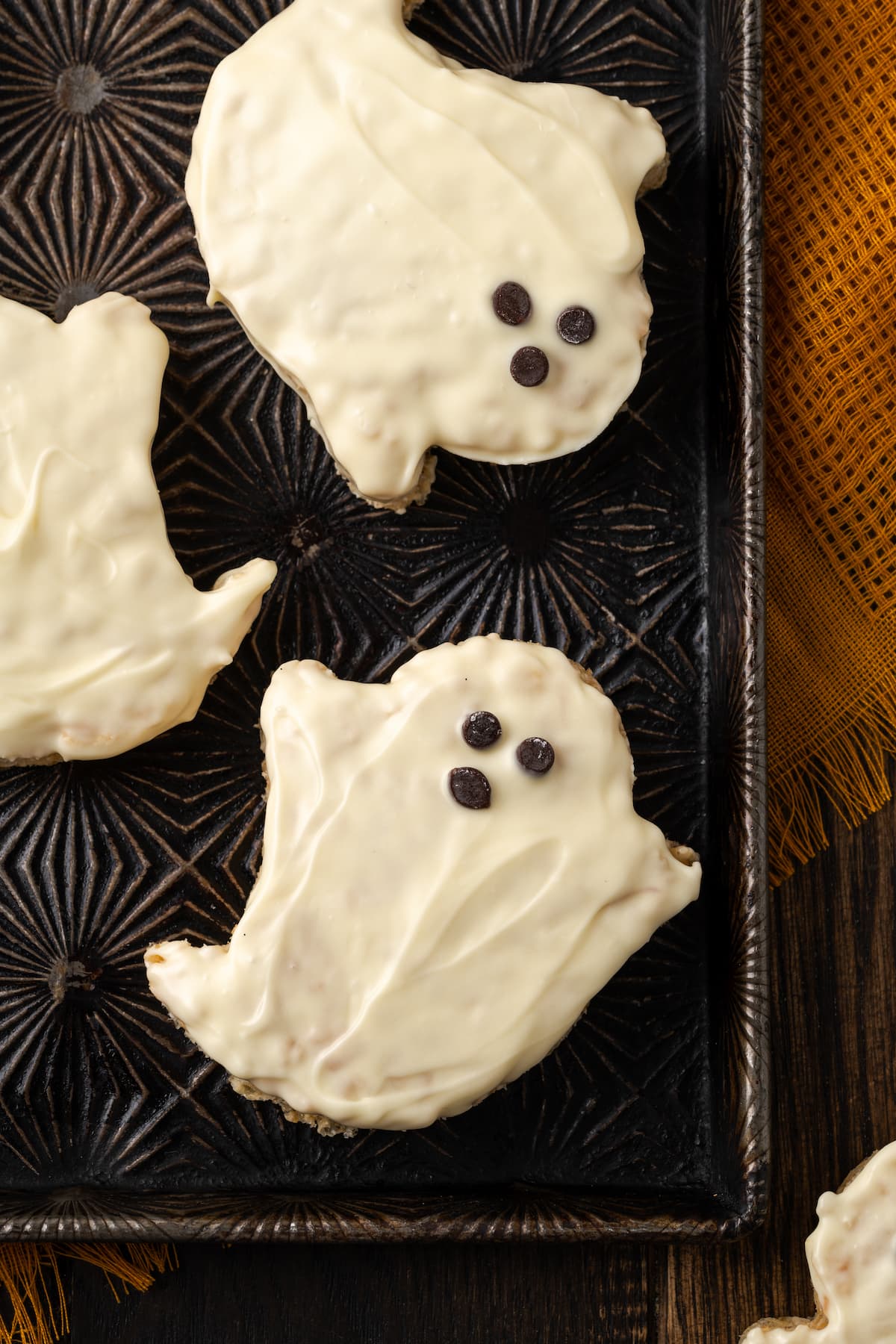 Close up of Halloween rice krispie treat ghosts dipped in white chocolate on a baking sheet, decorated with faces made from mini chocolate chips.