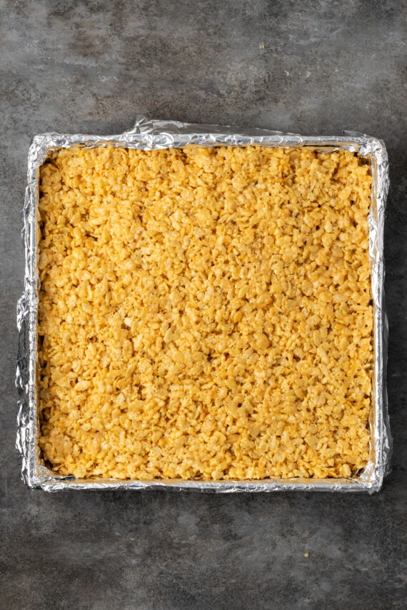 Peanut butter Rice Krispie marshmallow mixture pressed over a layer of Reese's peanut butter cups in a baking pan.