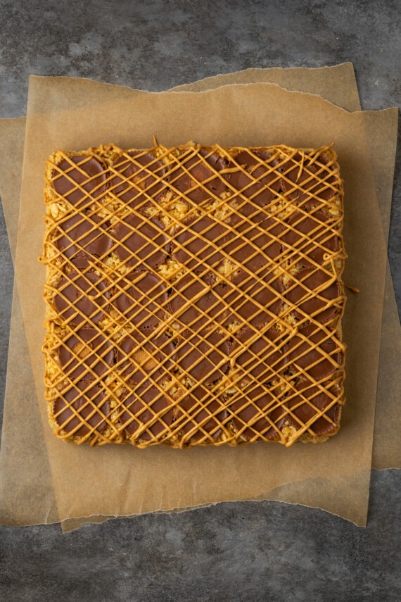 An uncut slab of peanut butter rice krispie treats topped with peanut butter cups and drizzled with melted peanut butter chips.