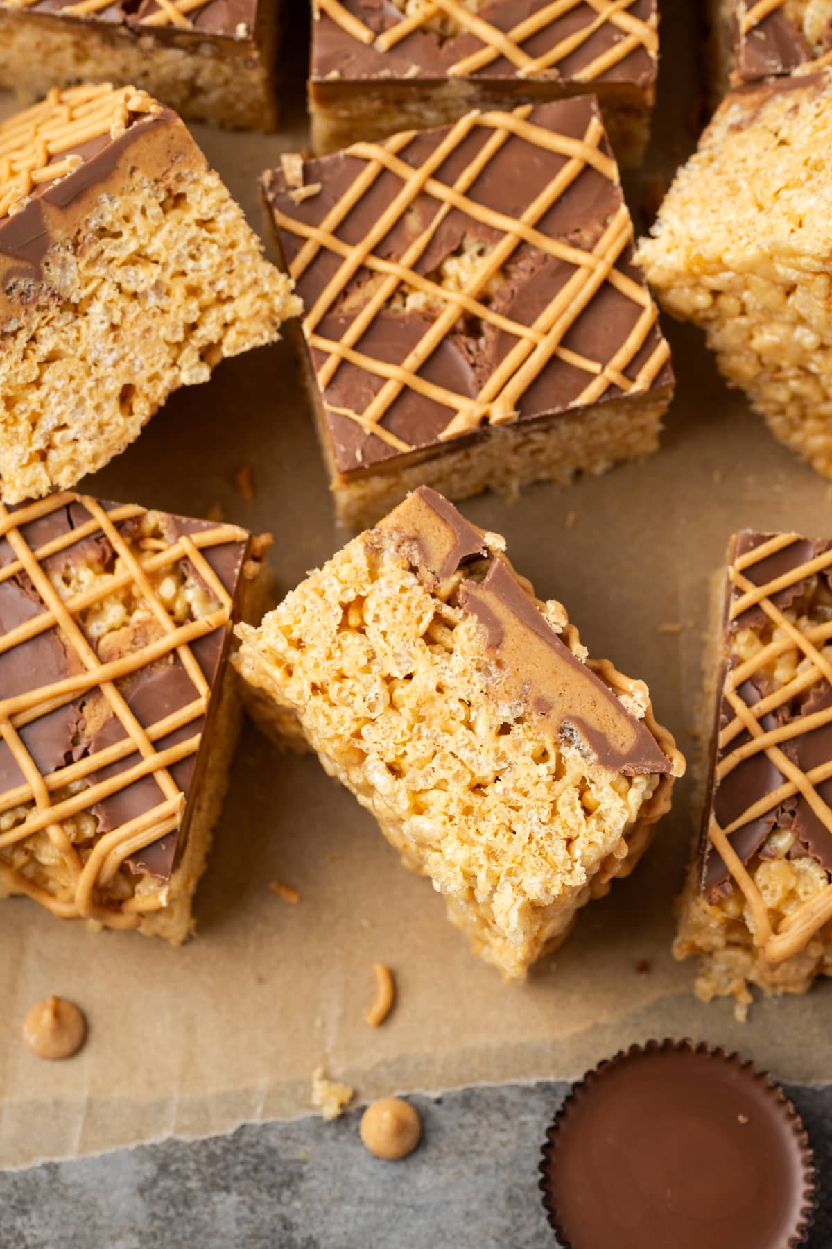 Overhead view of assorted peanut butter rice krispie treats drizzled with melted peanut butter chips, next to a peanut butter cup.