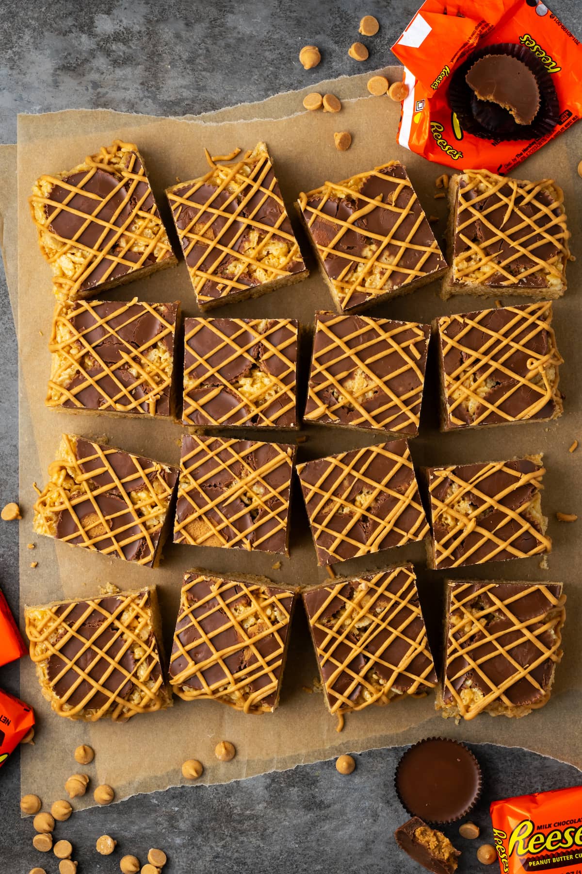 Overhead view of peanut butter rice krispie treats cut into squares next to partially unwrapped Reese's peanut butter cups.