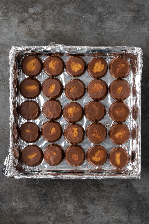Reese's peanut butter cups arranged in the bottom of a square foil-lined baking pan.