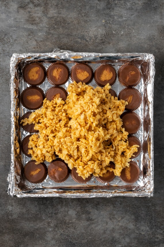 Peanut butter Rice Krispie marshmallow mixture added to a baking pan over a layer of Reese's peanut butter cups.