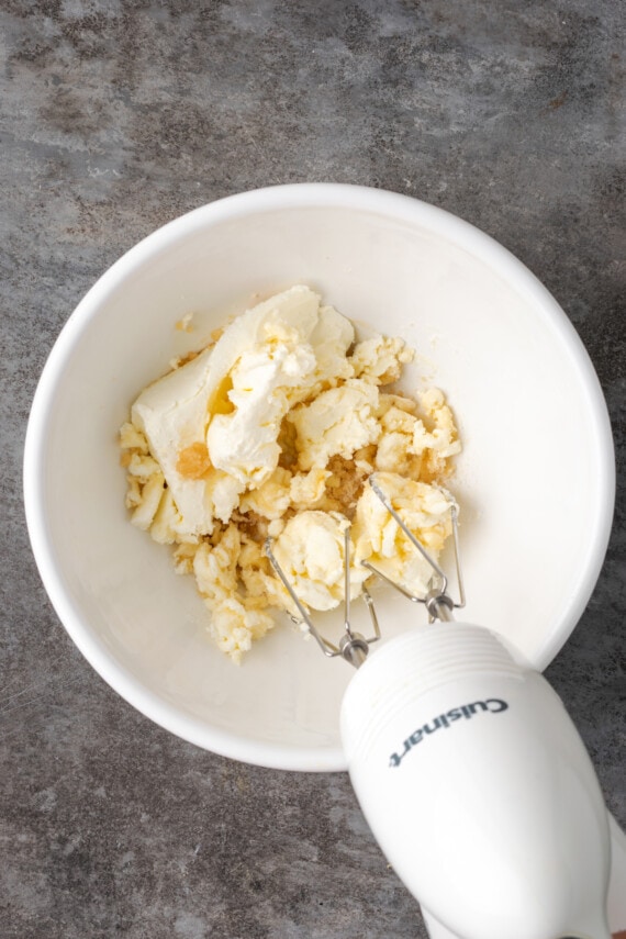 Sugar, cream cheese, and vanilla being blended in a bowl.