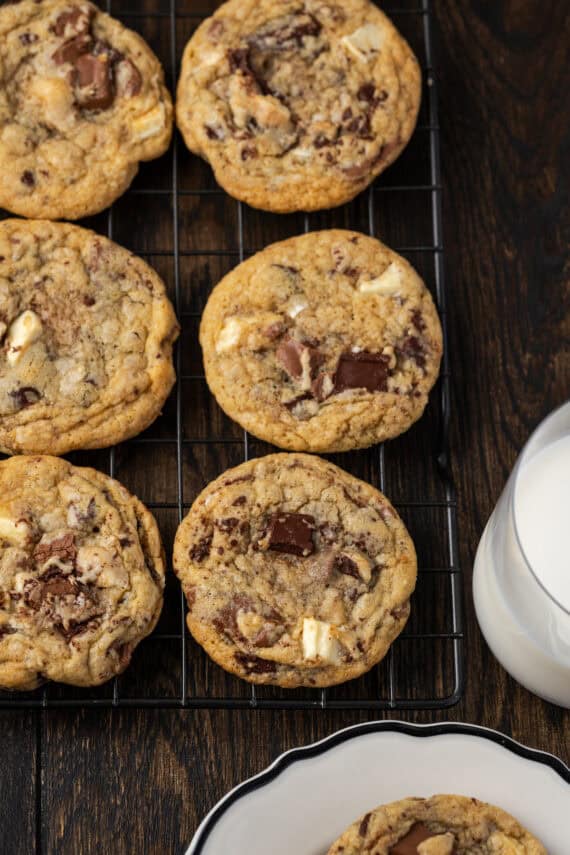 Overhead close up view of rows of triple chocolate cookies on a wire rack, next to a glass of milk.