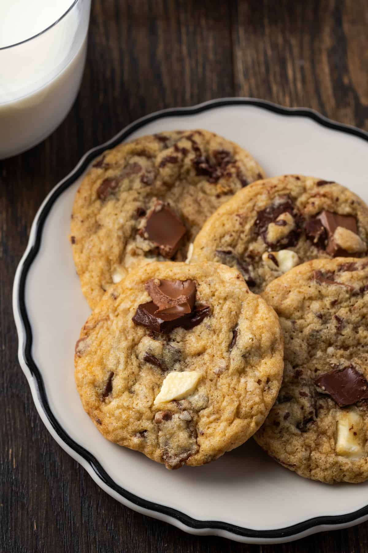 Triple chocolate cookies stacked on a white plate next to a glass of milk.