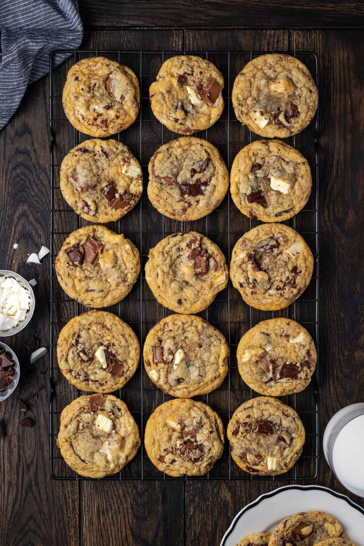 Overhead view of rows of triple chocolate cookies on a wire rack, next to a glass of milk.