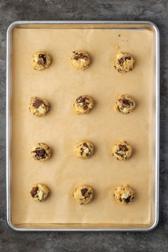 Overhead view of rows of triple chocolate cookie dough balls on a parchment-lined baking sheet.