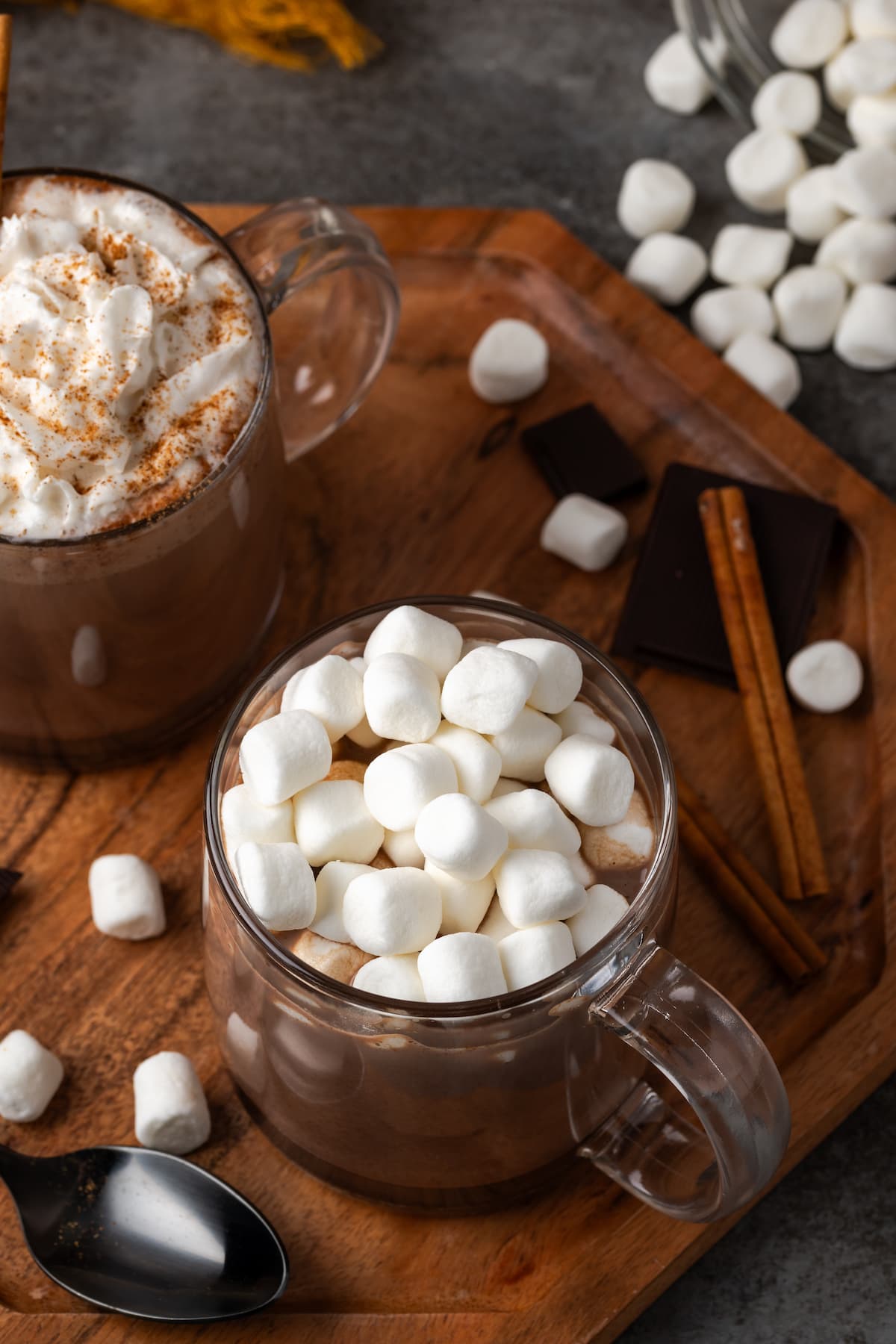 A mug of pumpkin spice hot chocolate topped with marshmallows next to a second mug garnished with whipped cream and cinnamon.