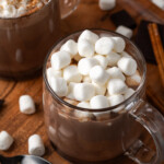 A mug of pumpkin spice hot chocolate topped with marshmallows next to a second mug garnished with whipped cream and cinnamon.