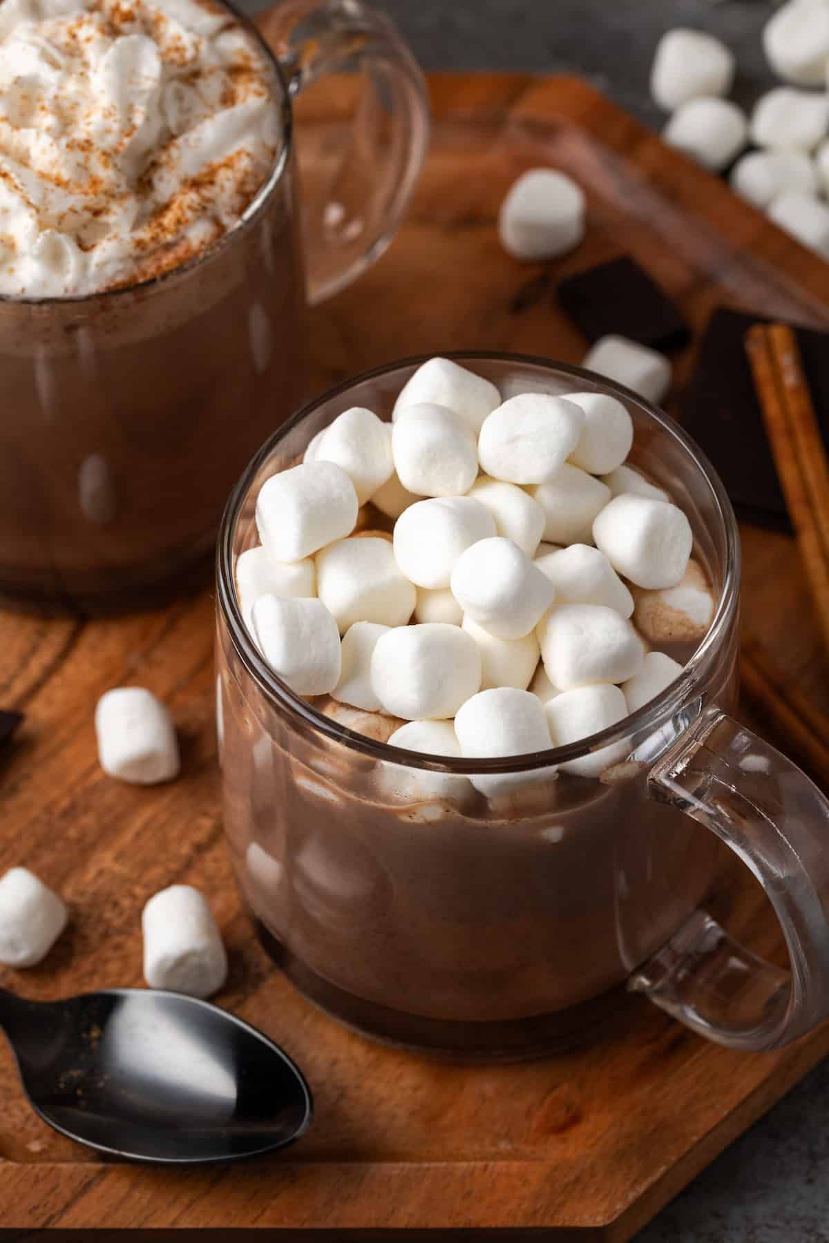 A mug of pumpkin spice hot chocolate topped with marshmallows next to a second mug garnished with whipped cream and cinnamon.
