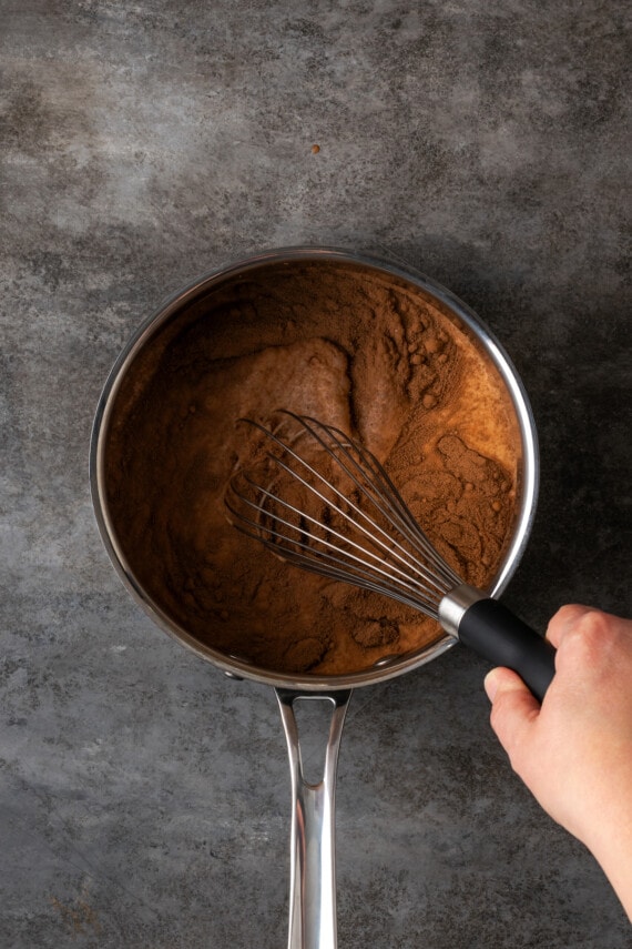 Hot chocolate mix is whisked with warm milk in a saucepan.