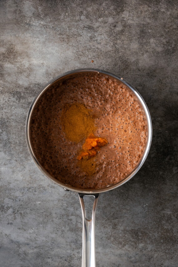 Pumpkin puree added to hot chocolate in a saucepan.