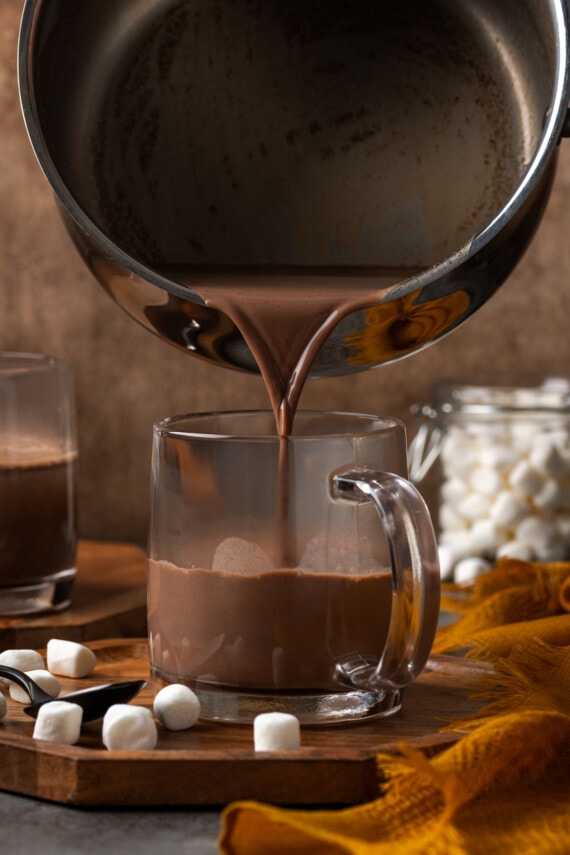 Pumpkin spice hot chocolate poured from a saucepan into a glass mug.