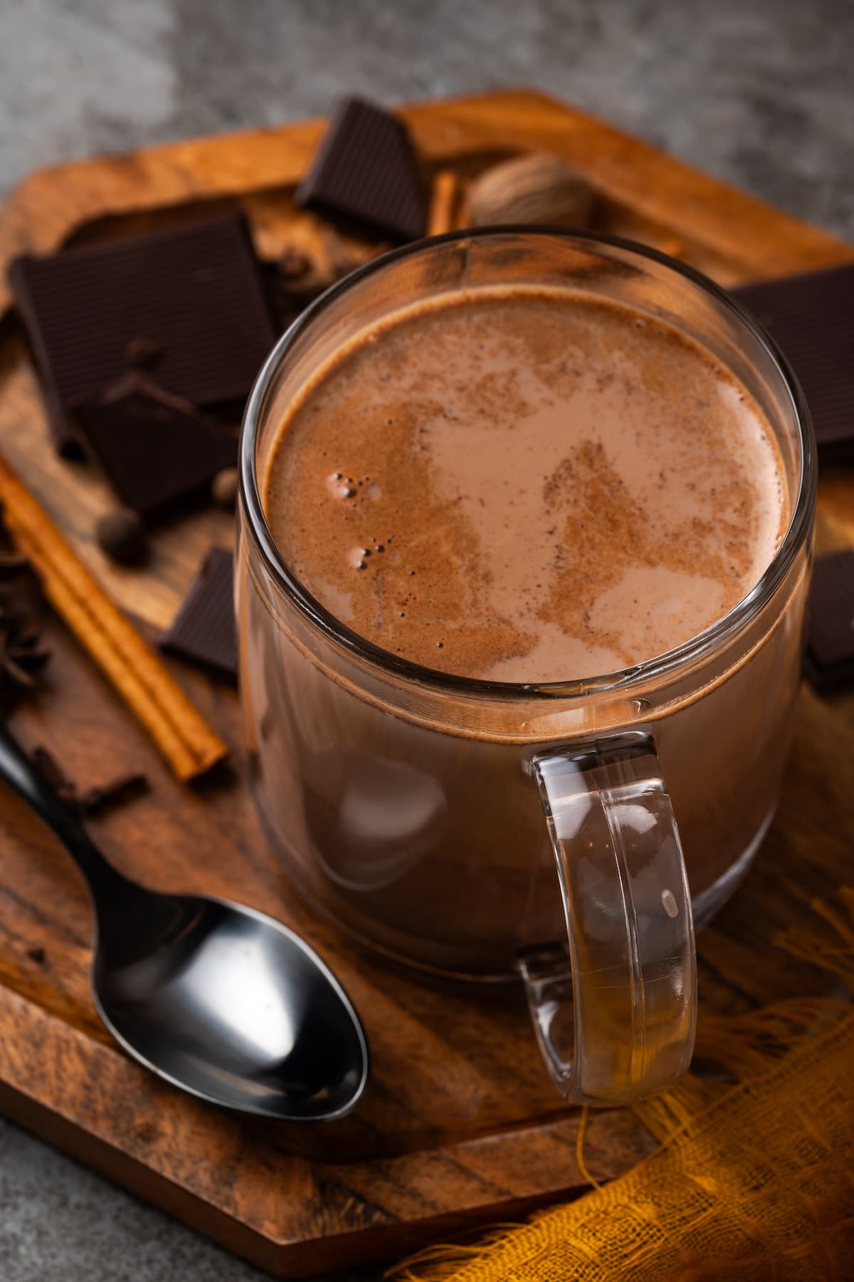 Pumpkin spice hot chocolate in a glass mug next to a spoon.