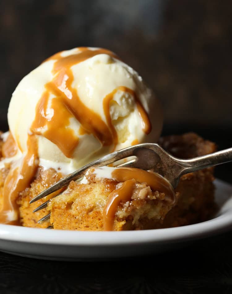 A fork stuck in a slice of pumpkin cake with a scoop of ice cream and caramel sauce.