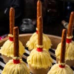 Witch's broom Halloween cupcakes on a wooden platter lined with black and white striped paper.