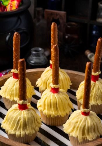 Witch's broom Halloween cupcakes on a wooden platter lined with black and white striped paper.