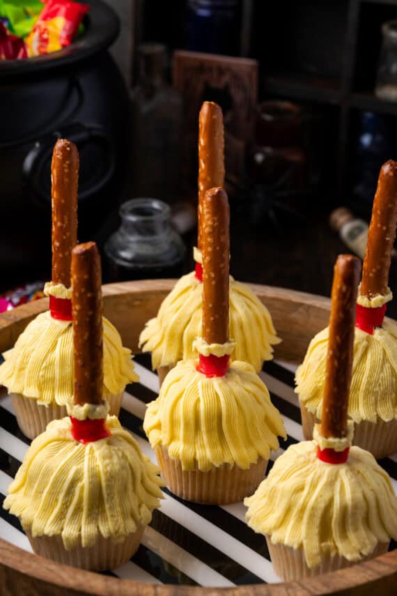 Witch's broom Halloween cupcakes on a wooden tray lined with black and white striped paper.