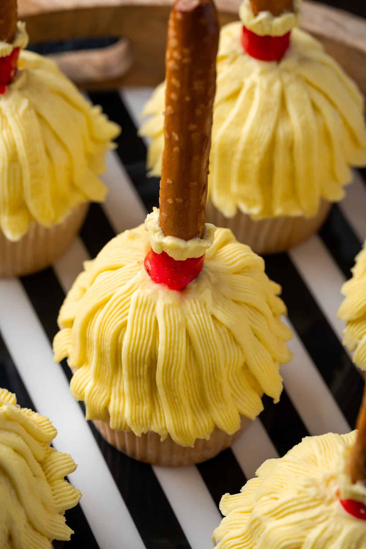 Close up of witches broom Halloween cupcakes on a wooden tray lined with black and white striped paper.