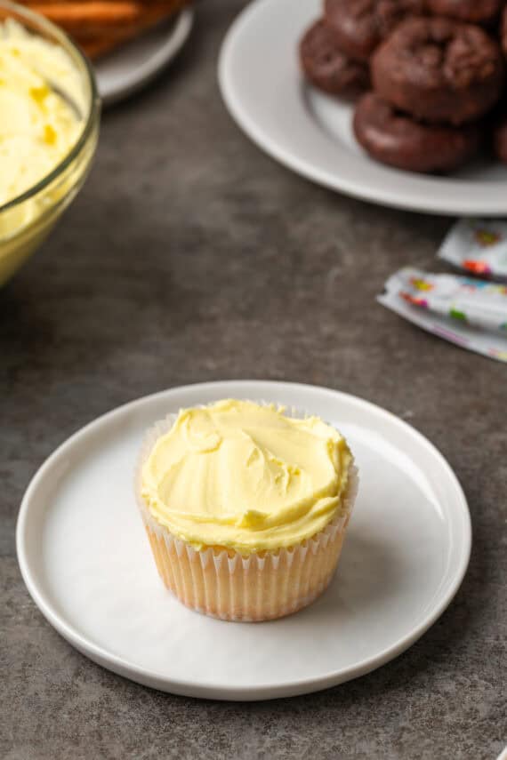 A cupcake frosted with yellow frosting on a white plate.