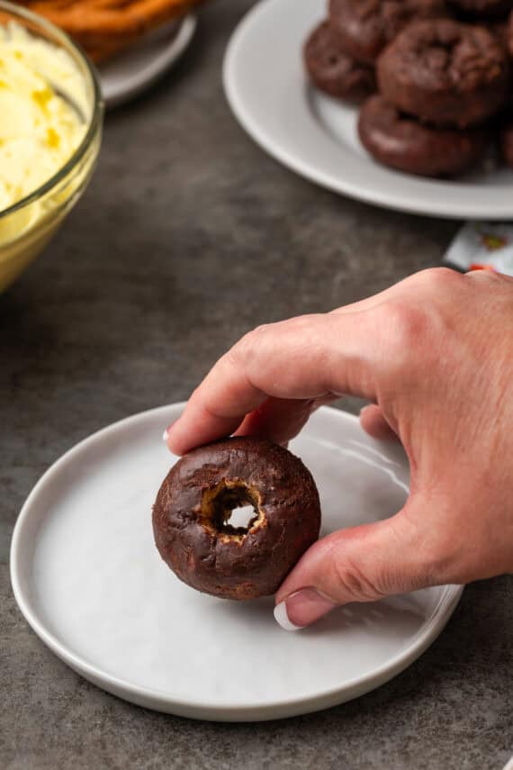 A mini donut is hollowed out through a hand on a white plate.