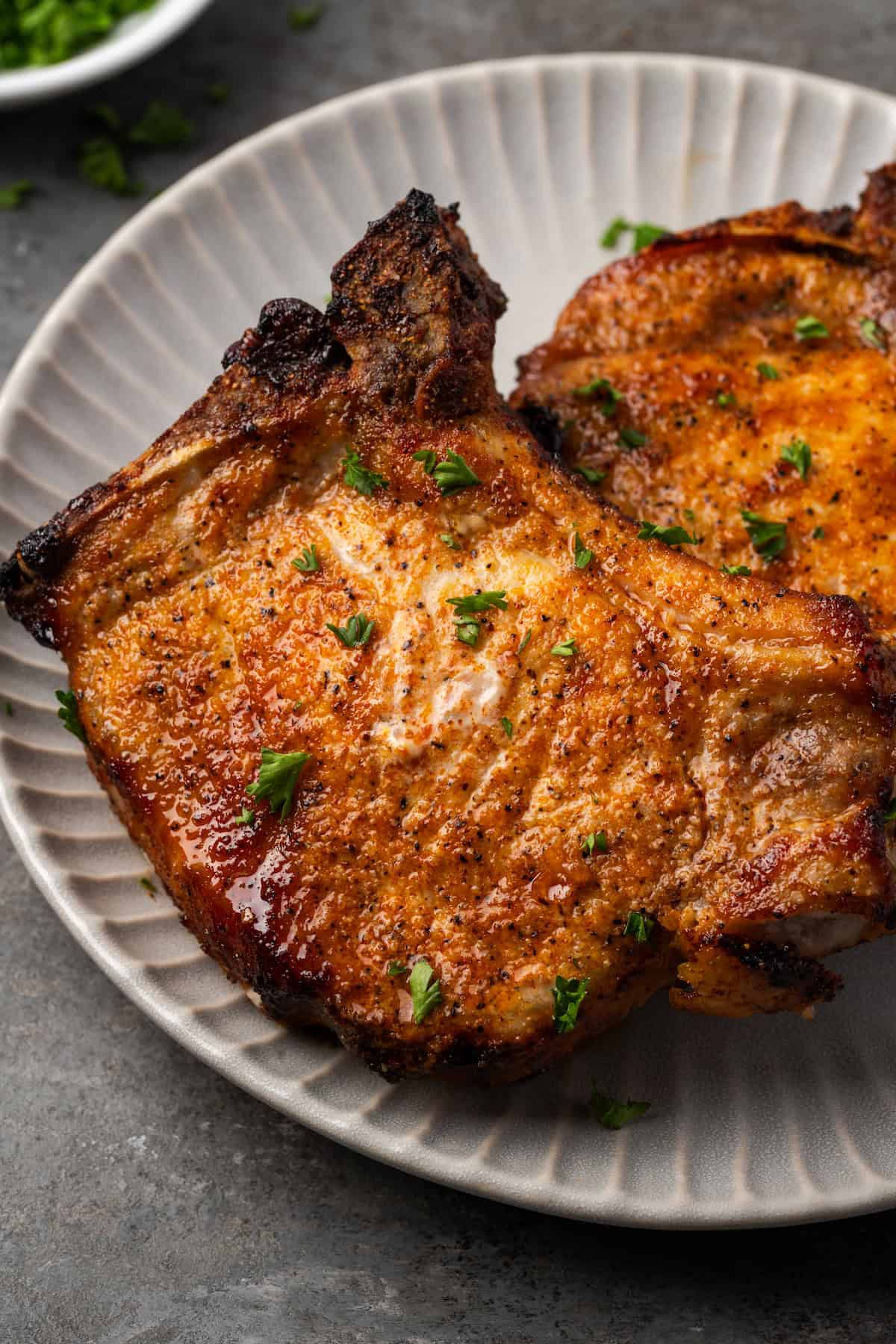 Make quick, easy, and juicy air fryer pork chops in 20 minutes! These bone-in chops are perfectly seared with a flavorful, caramelized crust. Close up of air fryer pork chops on a plate.