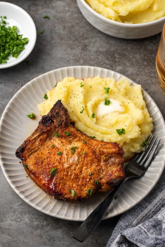 An air fryer pork chop next to mashed potatoes on a plate, with a fork.