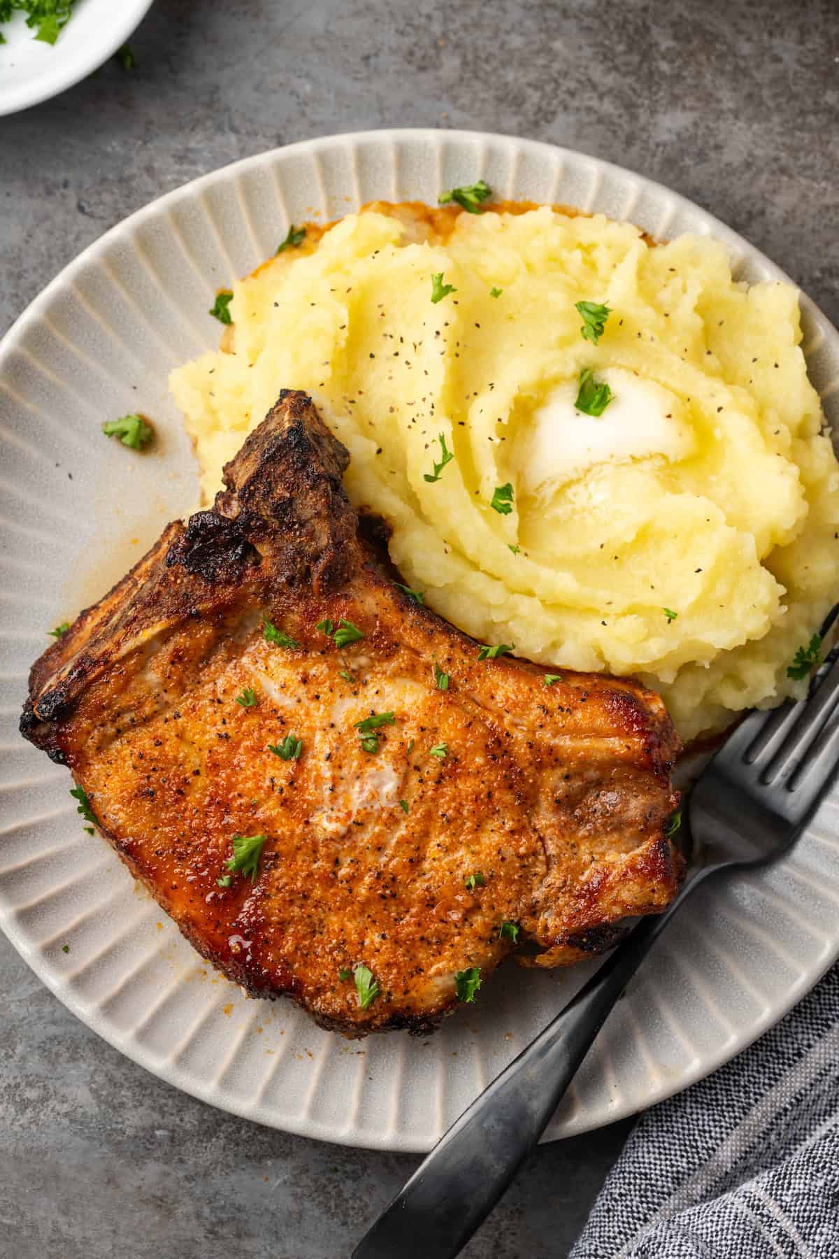 Make quick, easy, and juicy air fryer pork chops in 20 minutes! These bone-in chops are perfectly seared with a flavorful, caramelized crust. Overhead view of an air fryer pork chop next to mashed potatoes on a plate, with a fork.
