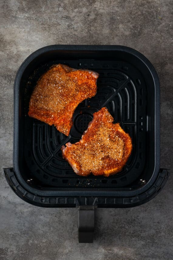 Make quick, easy, and juicy air fryer pork chops in 20 minutes! These bone-in chops are perfectly seared with a flavorful, caramelized crust. Overhead view of two uncooked seasoned pork chops inside the air fryer.