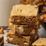 Three butterscotch blondies stacked next to a glass of milk.