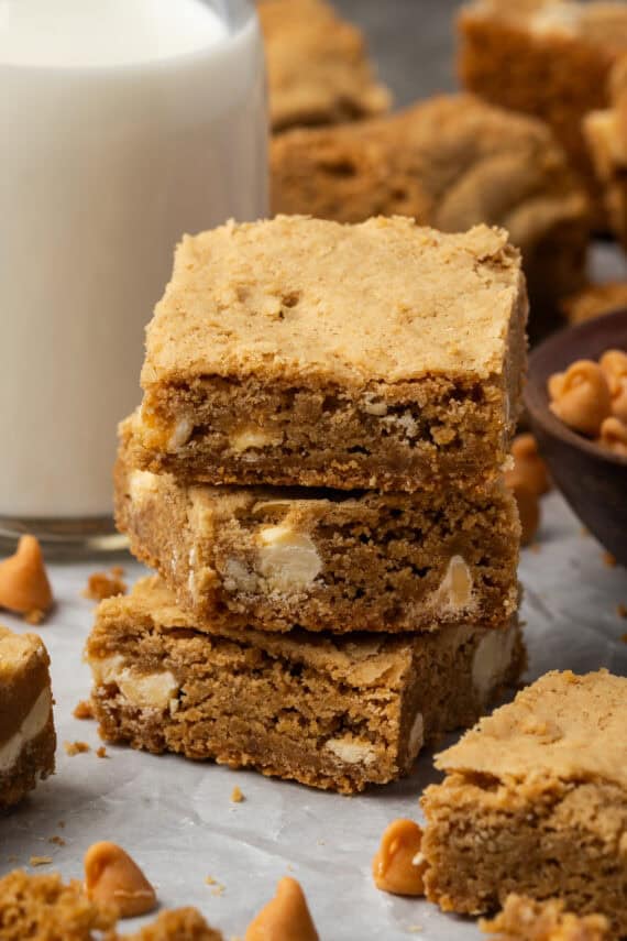 Three butterscotch blondies stacked next to a glass of milk.