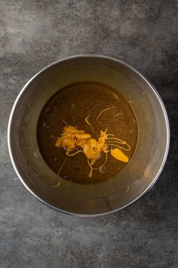 Melted butterscotch chips added to creamed wet ingredients inside a metal bowl.