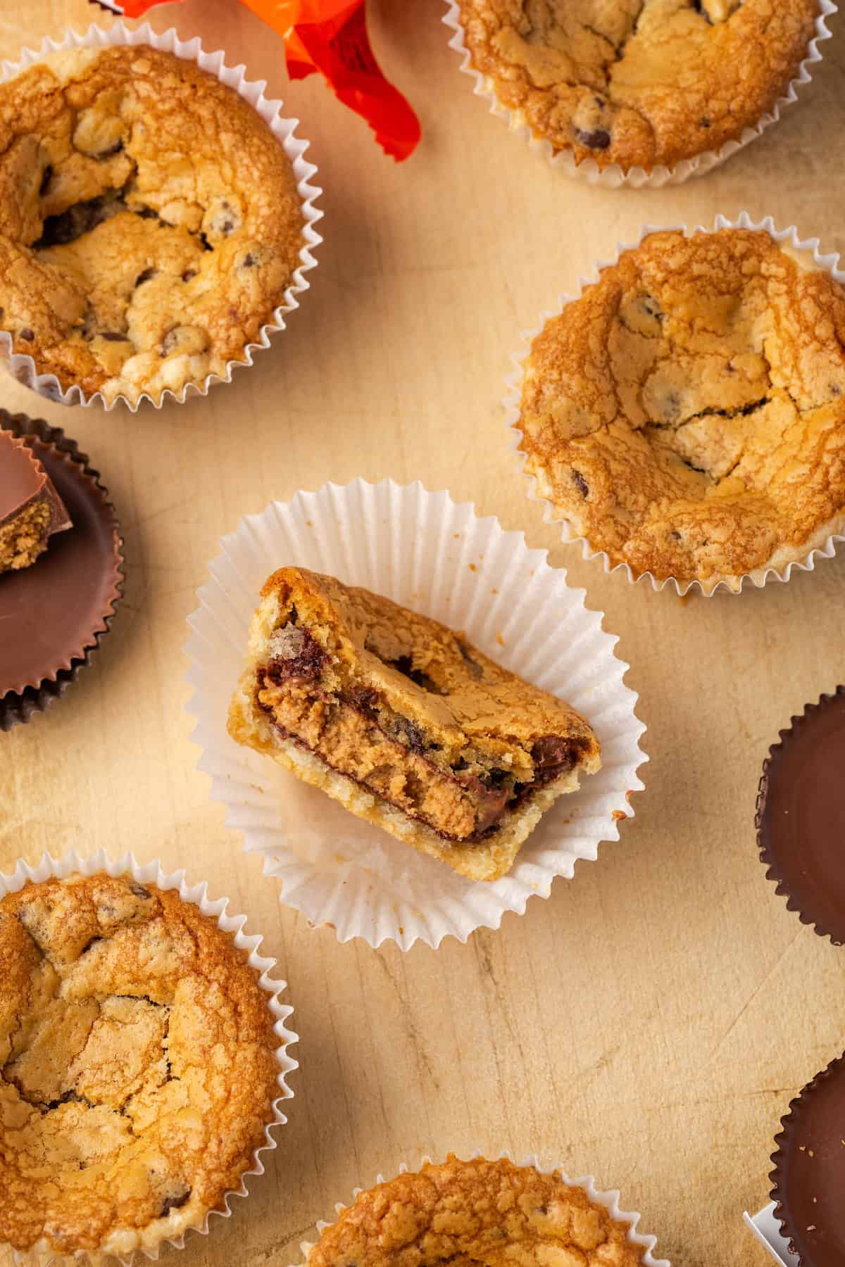 These are the ultimate cookie cups with two types of refrigerated cookie dough baked around a fudgy peanut butter cup. Quick and easy to make! Overhead view of a cookie cup with a bite missing inside a cupcake wrapper, surrounded by more cookie cups.
