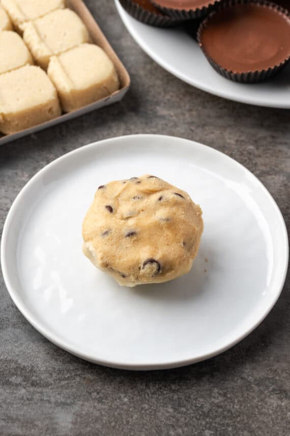 An assembled cookie cup made from chocolate chip cookie dough and sugar cookie dough wrapped around a Reese's peanut butter cup on a plate.