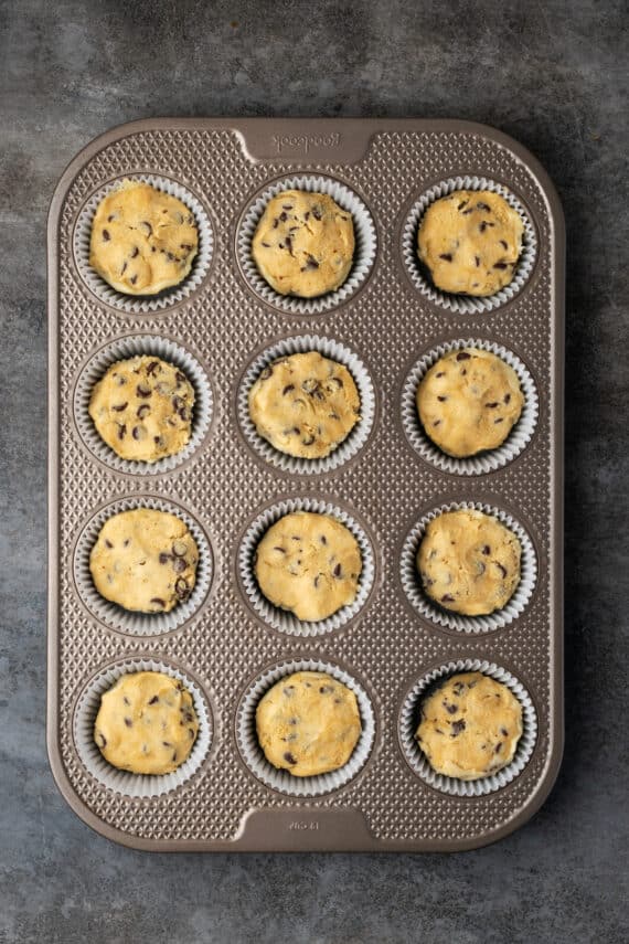 These are the ultimate cookie cups with two types of refrigerated cookie dough baked around a fudgy peanut butter cup. Quick and easy to make! Overhead view of unbaked cookie cups inside a 12-well muffin tin.