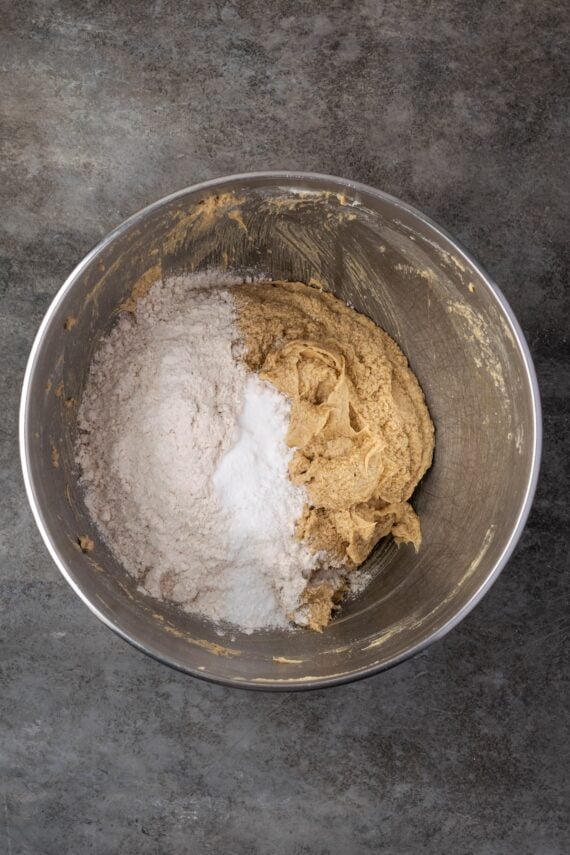 Dry ingredients added to cookie dough in a mixing bowl.