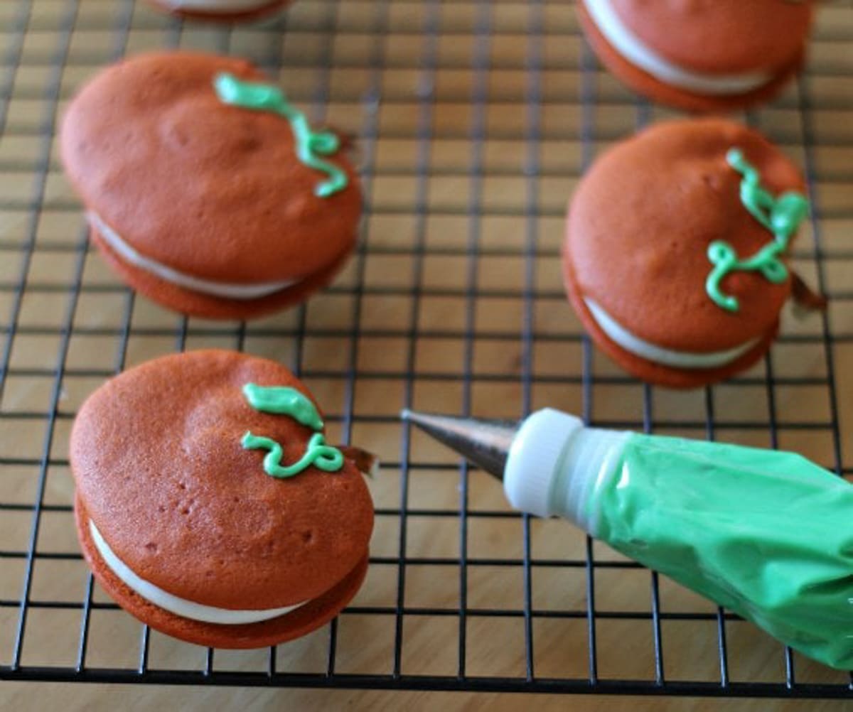 Piping green frosting into vines on a pumpkin whoopie pie