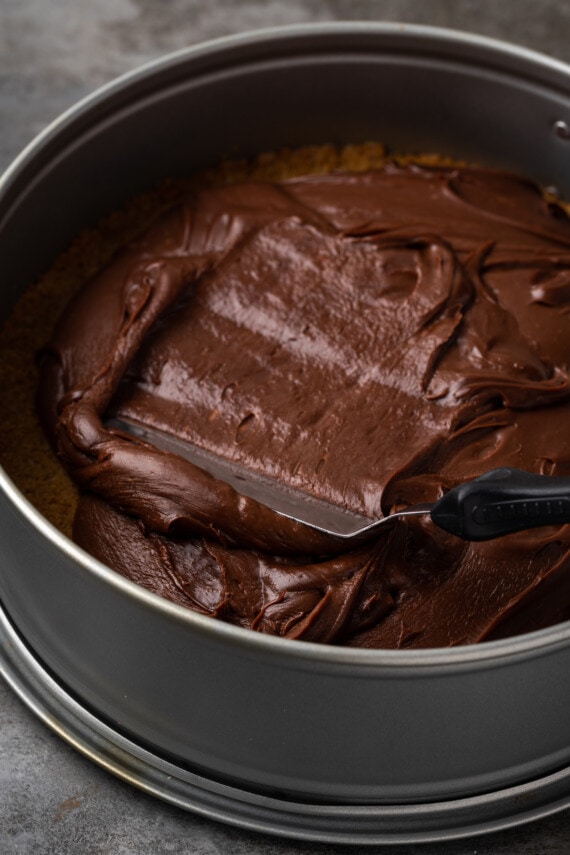 An offset spatula spreads hot fudge into the bottom of a springform pan.