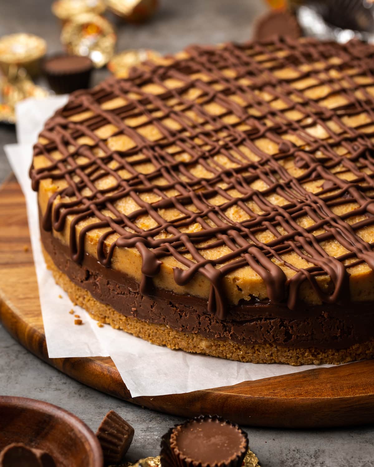 Reese's fudge pie topped with drizzles of chocolate sauce on a round wooden cutting board.